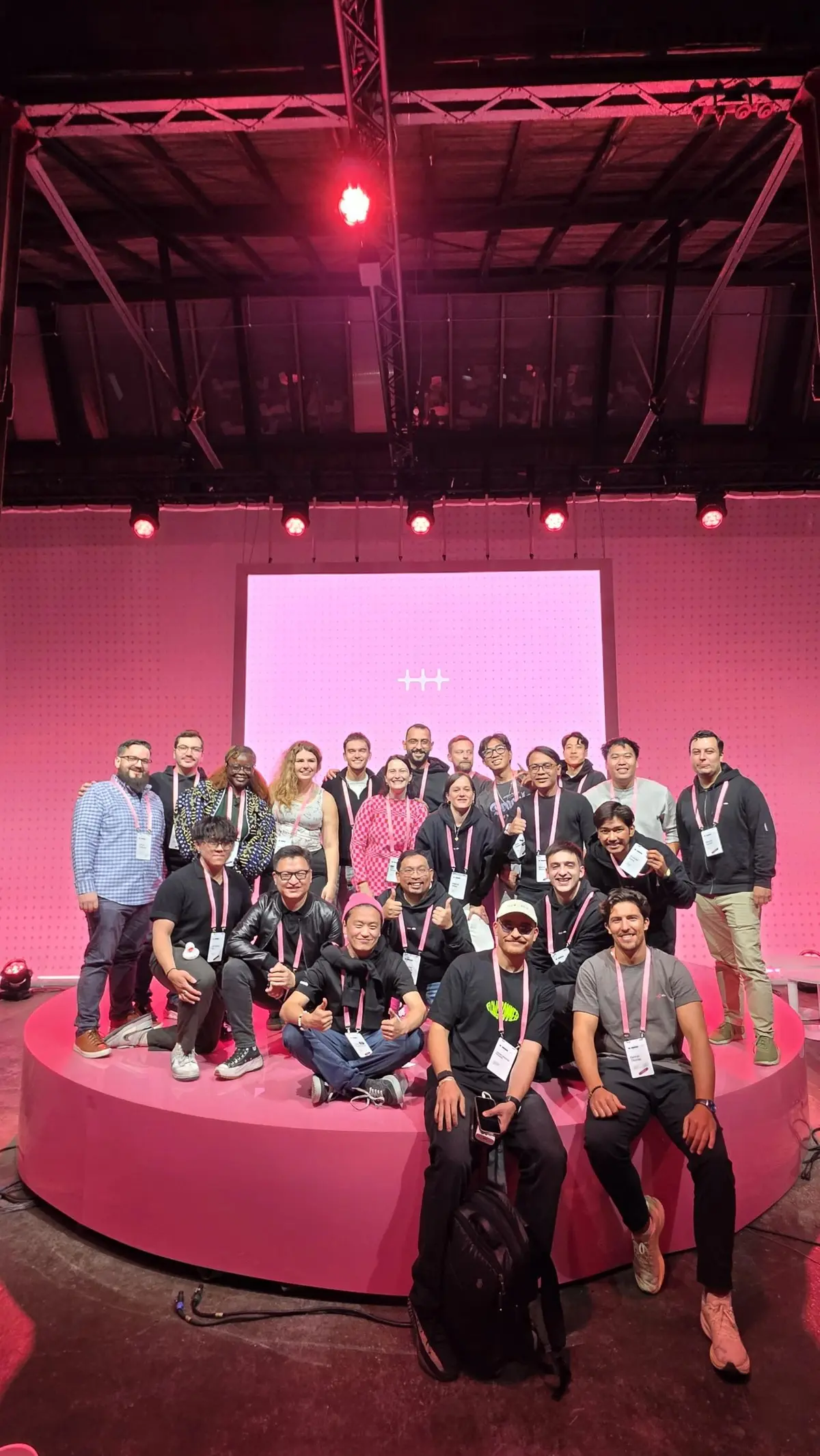 A group of n8n ambassadors posing together on the pink circular main stage at In The Loop 2026