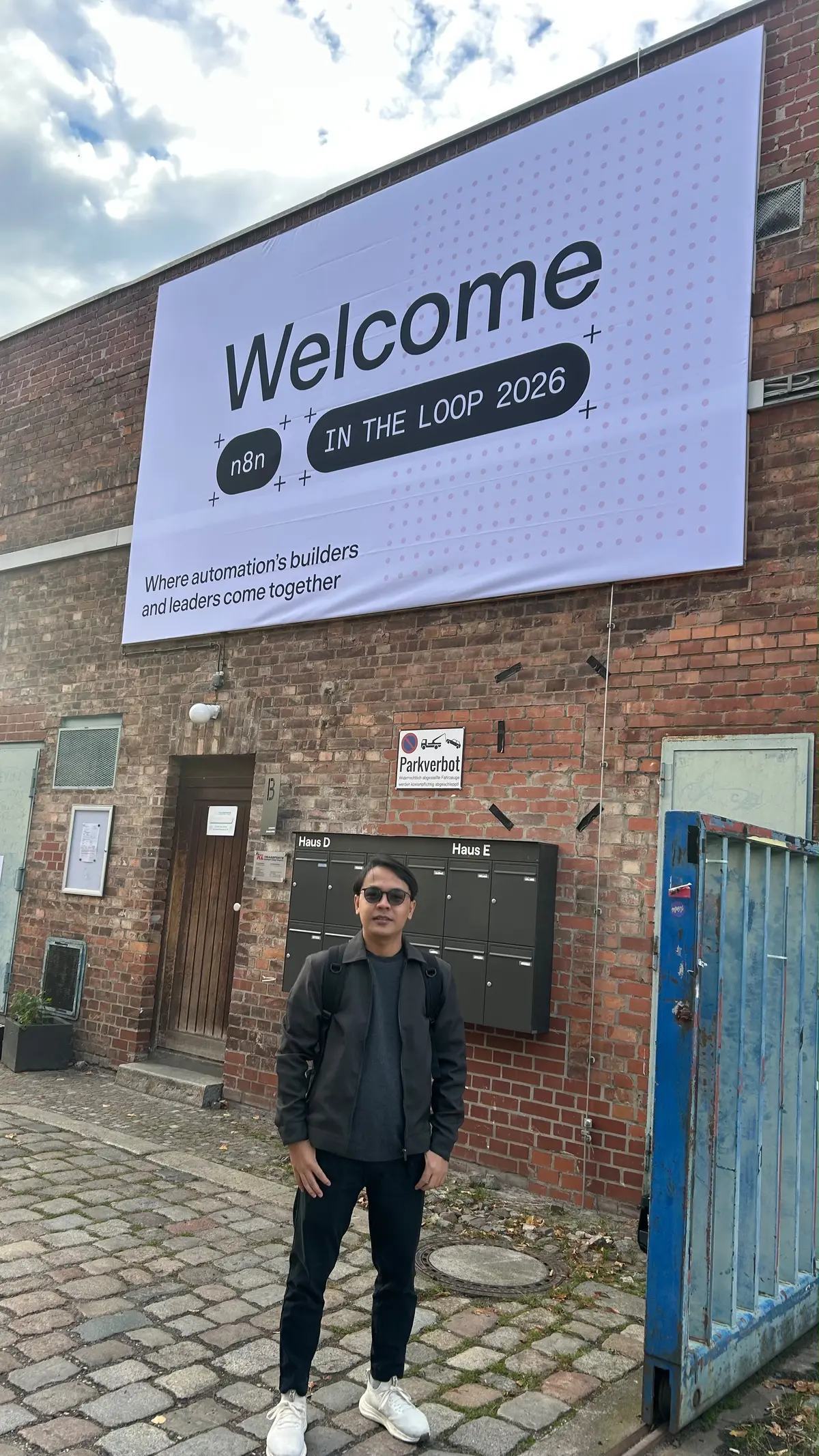 Khairul Muhtadin standing in front of the n8n In The Loop 2026 Welcome banner on a brick building in Berlin